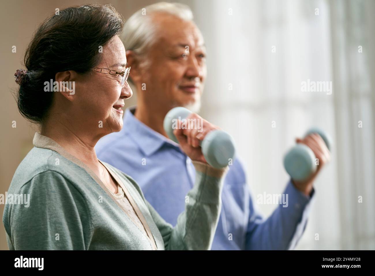 felice senior coppia asiatica esercizio a casa utilizzando manubri Foto Stock