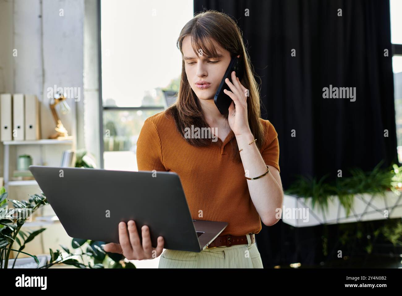 Persona concentrata impegnata in attività lavorative utilizzando un computer portatile durante una telefonata in ufficio. Foto Stock