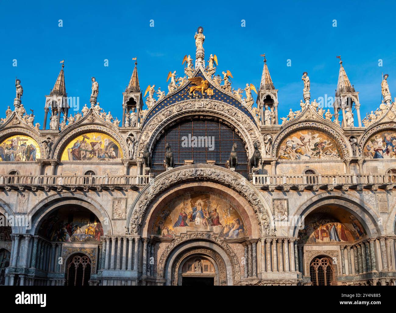 Facciata della Basilica della Cattedrale di San Marco con ingresso che splende alla luce del sole serale a Venezia in Europa contro il cielo azzurro senza nuvole Foto Stock