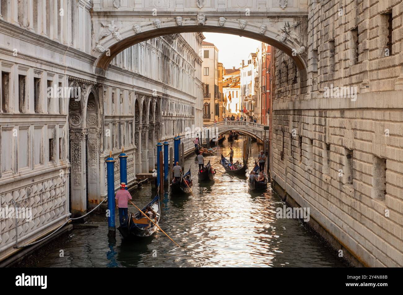 Vista posteriore dei gondolieri maschi che regnano lunghe e strette barche e attraversano il Ponte dei Sospiri tra gli edifici della città di Venezia Foto Stock