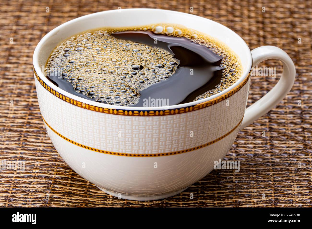 Una tazza di caffè nero. Vista ad angolo alto del caffè nero caldo con bolle d'aria in una bella tazza in ceramica marrone su un tappetino scuro. Foto Stock