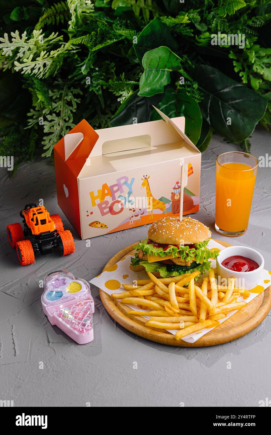 Allegro pasto per bambini con hamburger, patatine fritte e succo d'arancia accanto a un'auto giocattolo e a un telefono Foto Stock