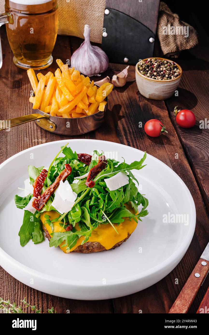 Delizioso cheeseburger con rucola e pomodori secchi su un tavolo rustico con contorni Foto Stock