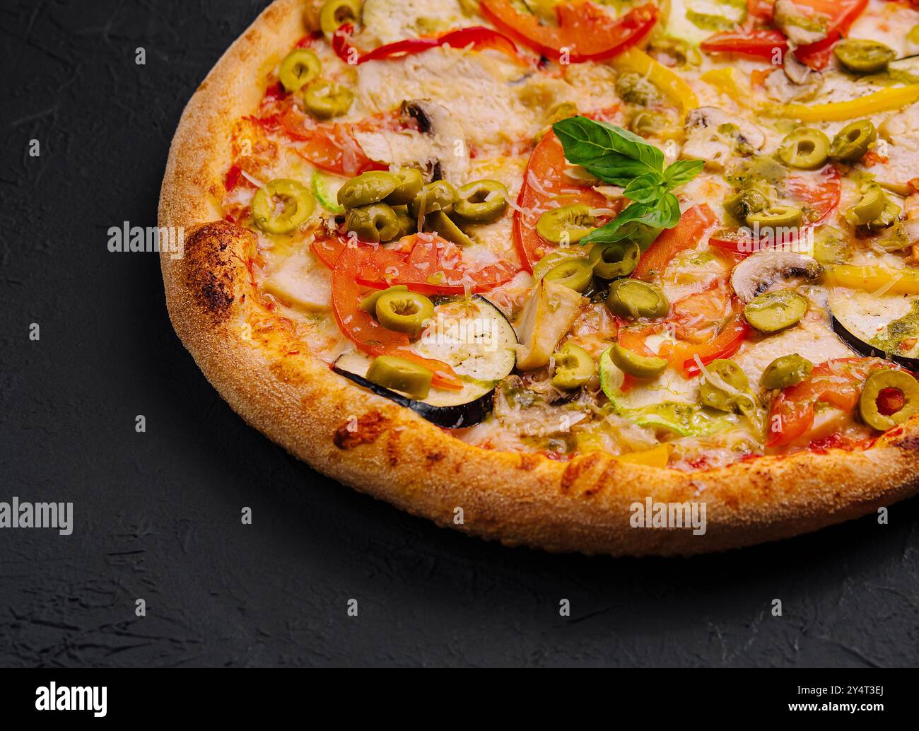 Vivace pizza vegetale con una varietà di condimenti su una superficie scura e ruvida Foto Stock