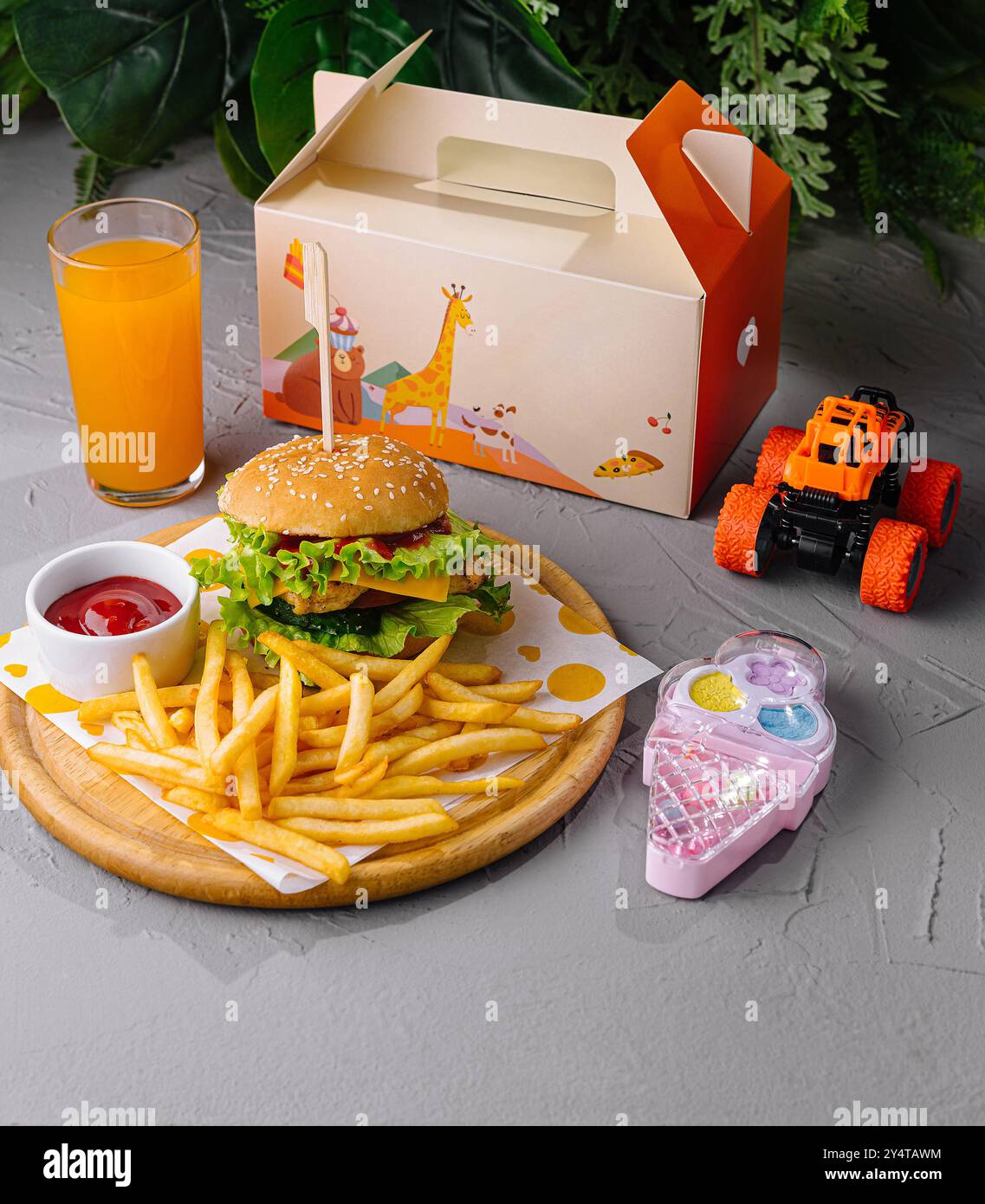 Allegro pasto per bambini con hamburger, patatine fritte e succo d'arancia accanto a un'auto giocattolo e a un telefono Foto Stock