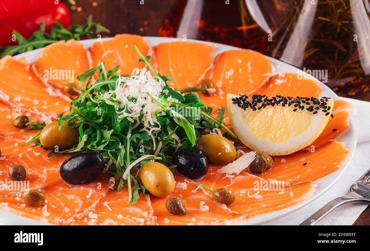 Antipasto al carpaccio di salmone guarnito con rucola fresca, olive, limone e capperi serviti sul tavolo del ristorante in legno Foto Stock