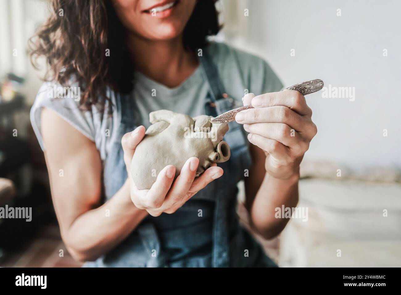 Ceramica d'arte, artista lavora con scultura in ceramica presso lo studio di laboratorio di argilla. Vista ritagliata, donna che scolpisce la forma del cuore. Piccole imprese e artigianato artigianale Foto Stock