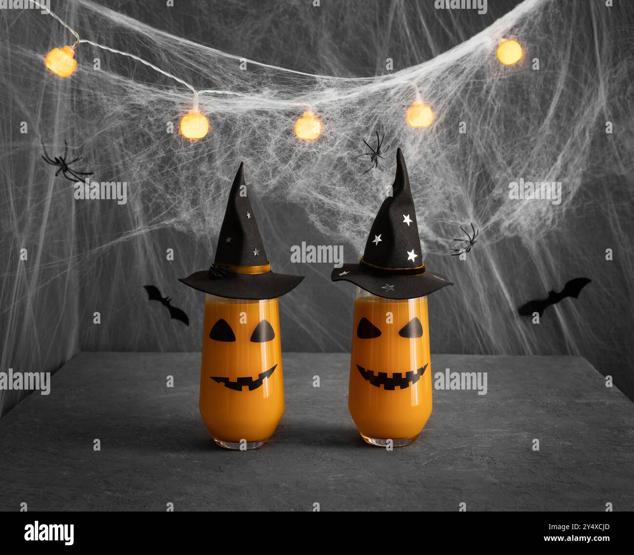 Bicchieri da cocktail di Halloween con faccia da jack lanterna in cappelli da strega neri su sfondo grigio con ragnatele. Serve per la festa di Halloween. Foto Stock