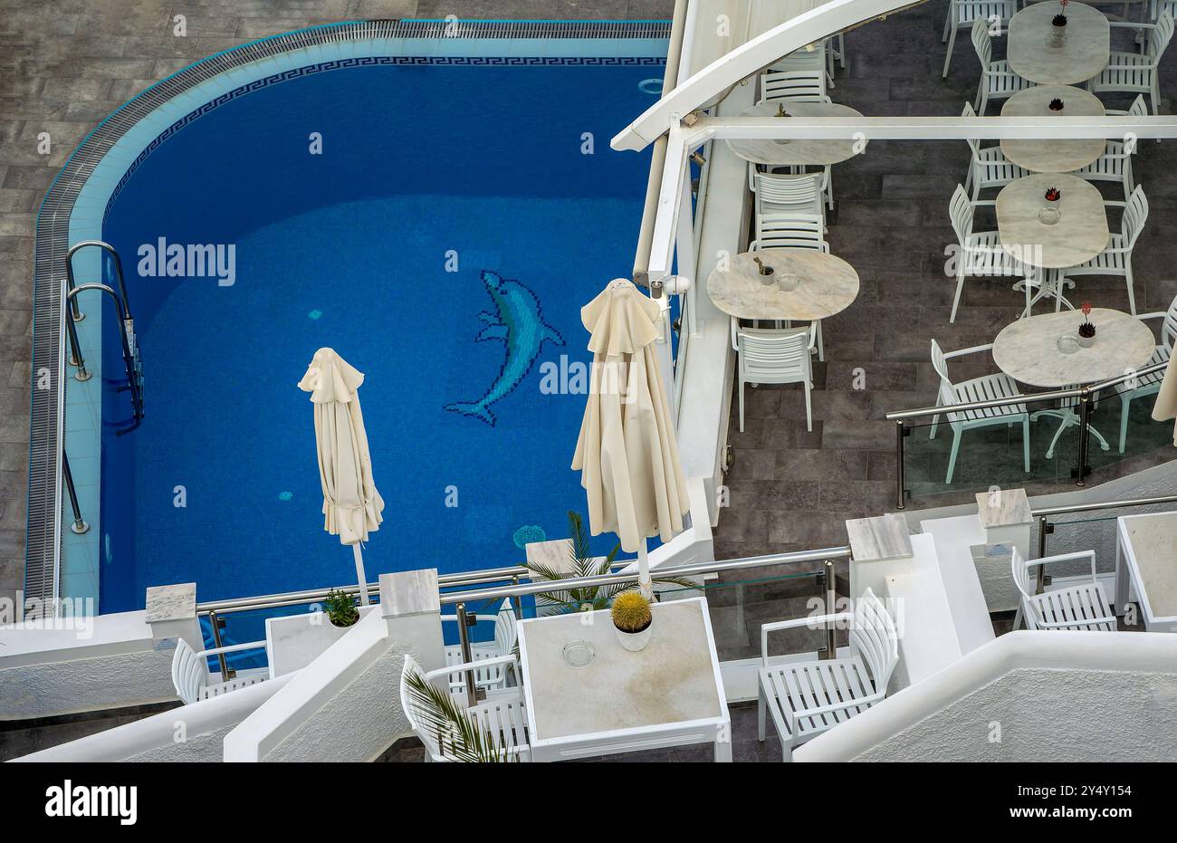 Piscina dell'hotel Fira con piastrelle di delfini, tavoli bianchi e sedie. Santorini, Grecia Foto Stock