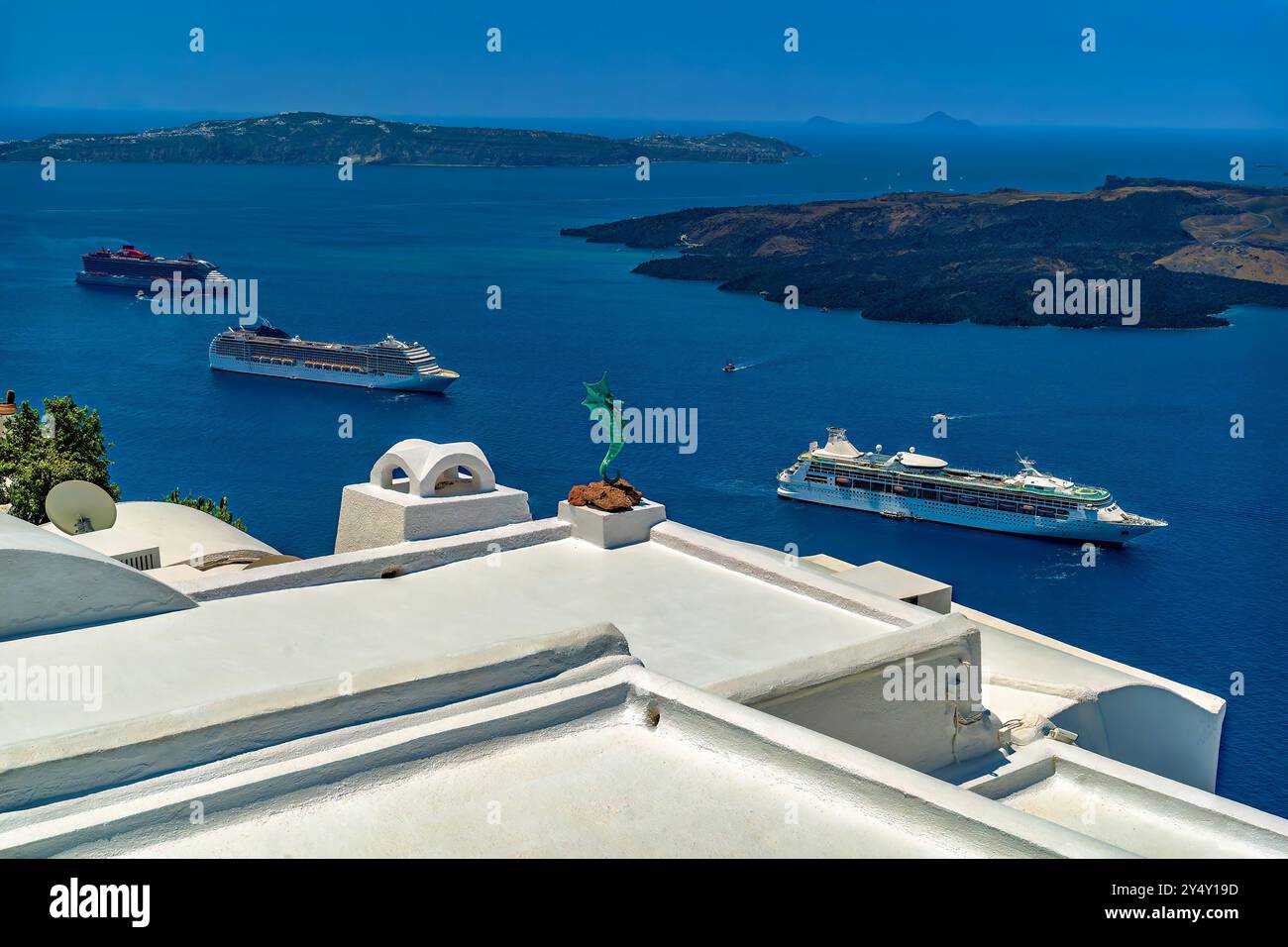 Vista mattutina della baia di Fira sull'isola di Santorini, in Grecia. Tetti bianchi, statua del cavalluccio marino, Nea Kameni e le lussuose navi da crociera nella baia Foto Stock