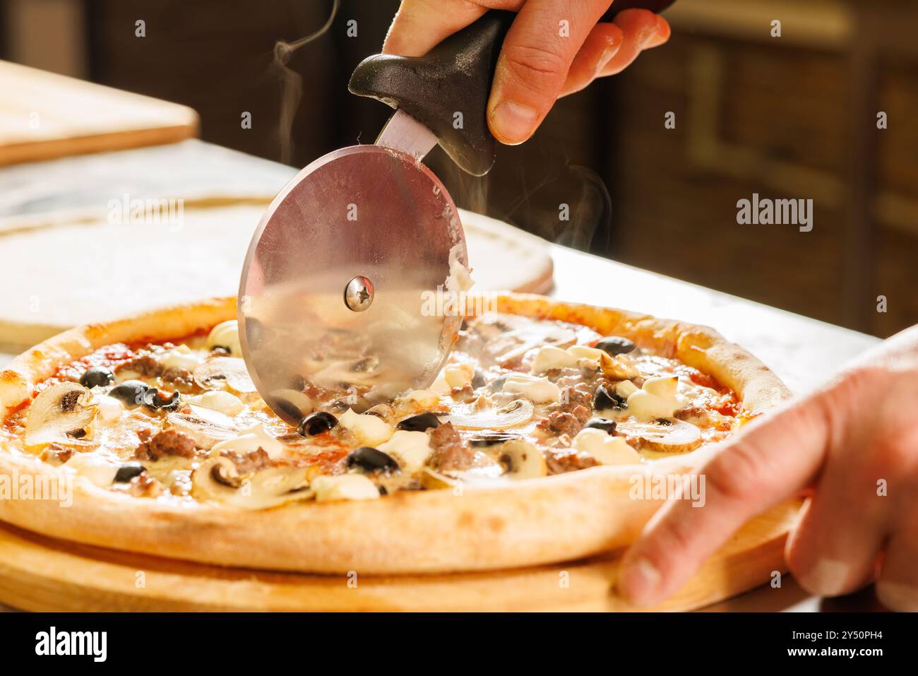 Primo piano di una persona che taglia una pizza appena sfornata con un tagliapiezzoli. La pizza ha condimenti che includono funghi, olive e formaggio. Foto Stock