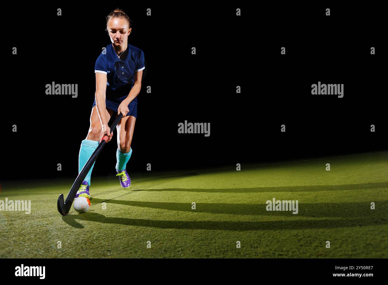 Giovane donna determinata che guida sapientemente la palla con il bastone da hockey su prato concentrato sul suo gioco. Isolato su sfondo nero Foto Stock