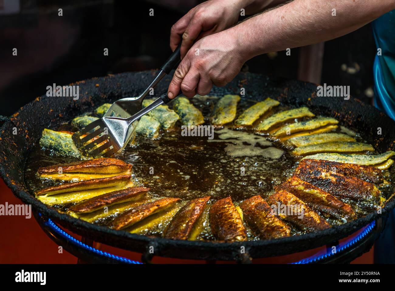Mani girano l'aringa fritta con una spatola in una grande padella di ghisa presso la affumiceria di pesce Föh a Kappeln, un'azienda a conduzione familiare dal 1911 le cui tre torri sono un punto di riferimento della città. Lusthof, Schleswig-Holstein, Germania. Foto Stock