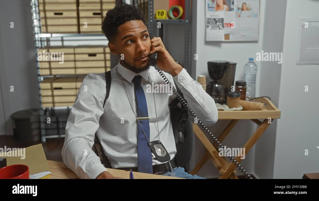 Bel detective afroamericano che parla al telefono nell'ufficio della stazione di polizia, circondato da prove investigative. Foto Stock