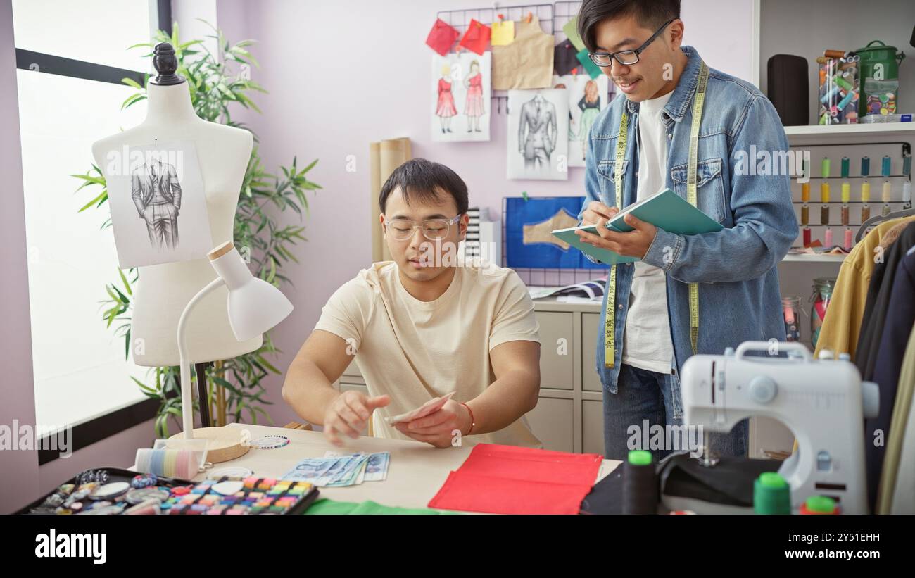 Due uomini asiatici che collaborano in un negozio di sartoria, con uno che disegna e l'altro che gestisce le note rmb. Foto Stock