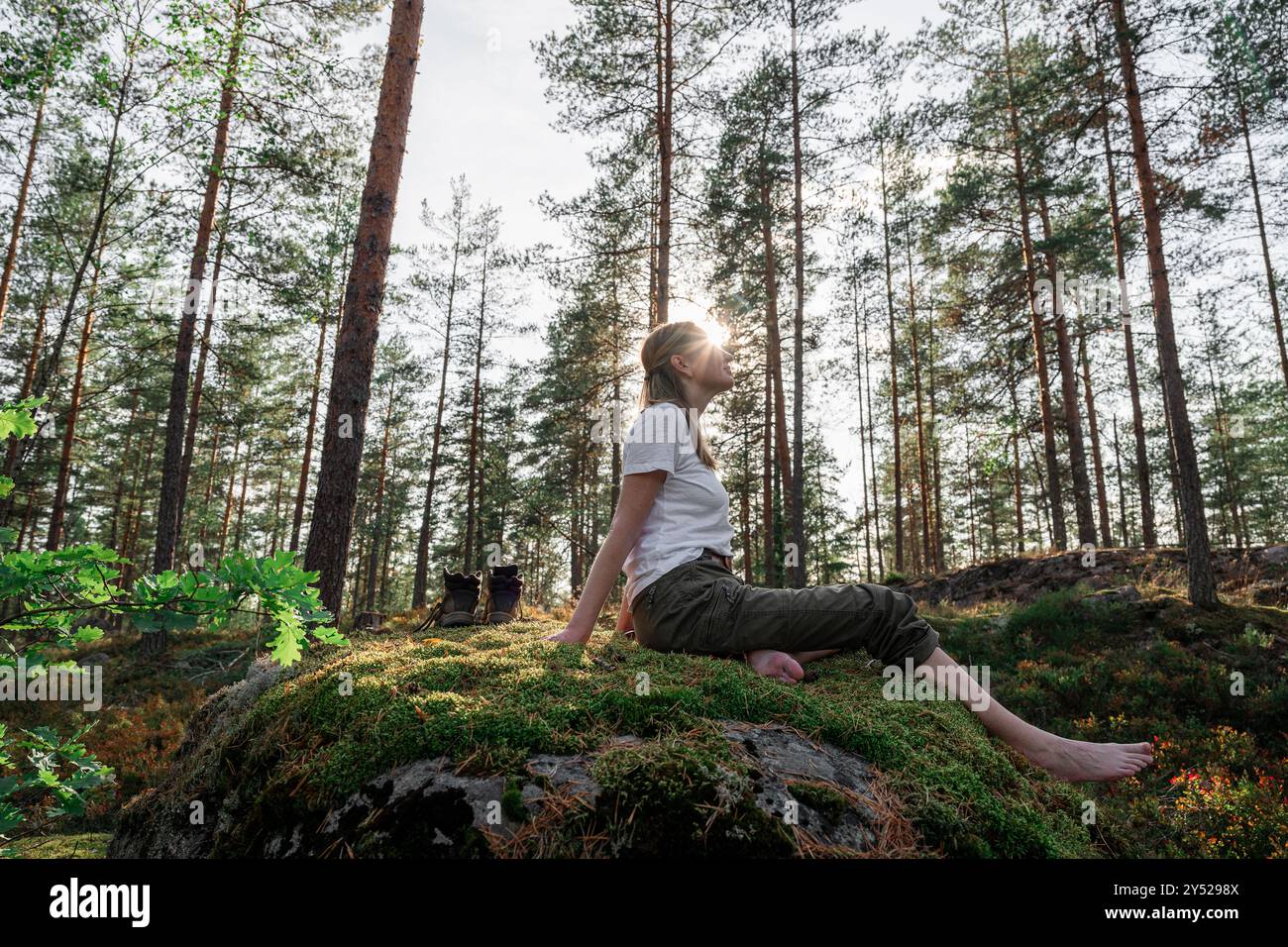 donna seduta su una pietra senza scarpe nella foresta autunnale alla luce del sole Foto Stock