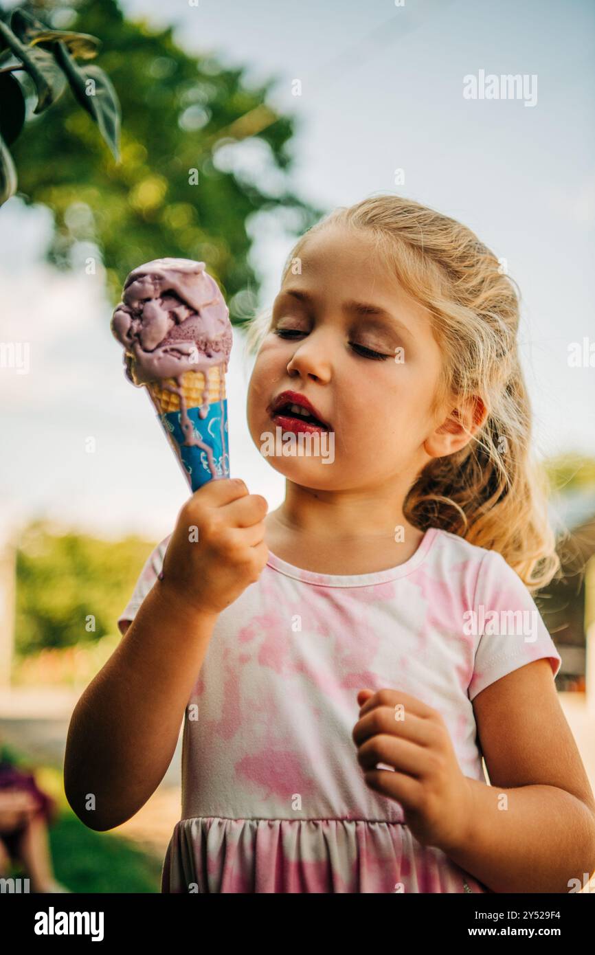 Una ragazza con un vestito rosa che si gode un cono di gelato viola Foto Stock