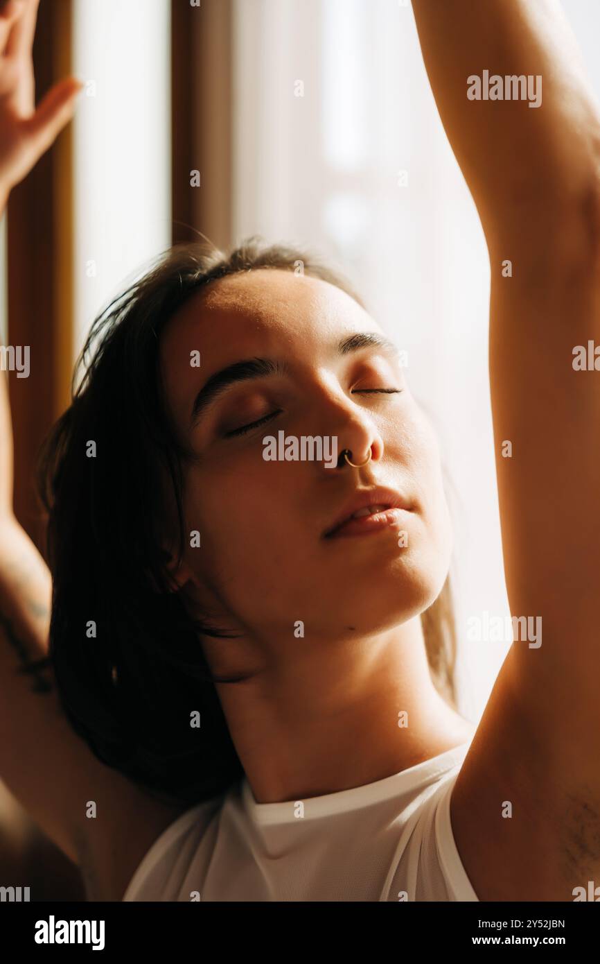 Donna crogiolata alla luce soffusa del sole, occhi chiusi con espressione serena Foto Stock