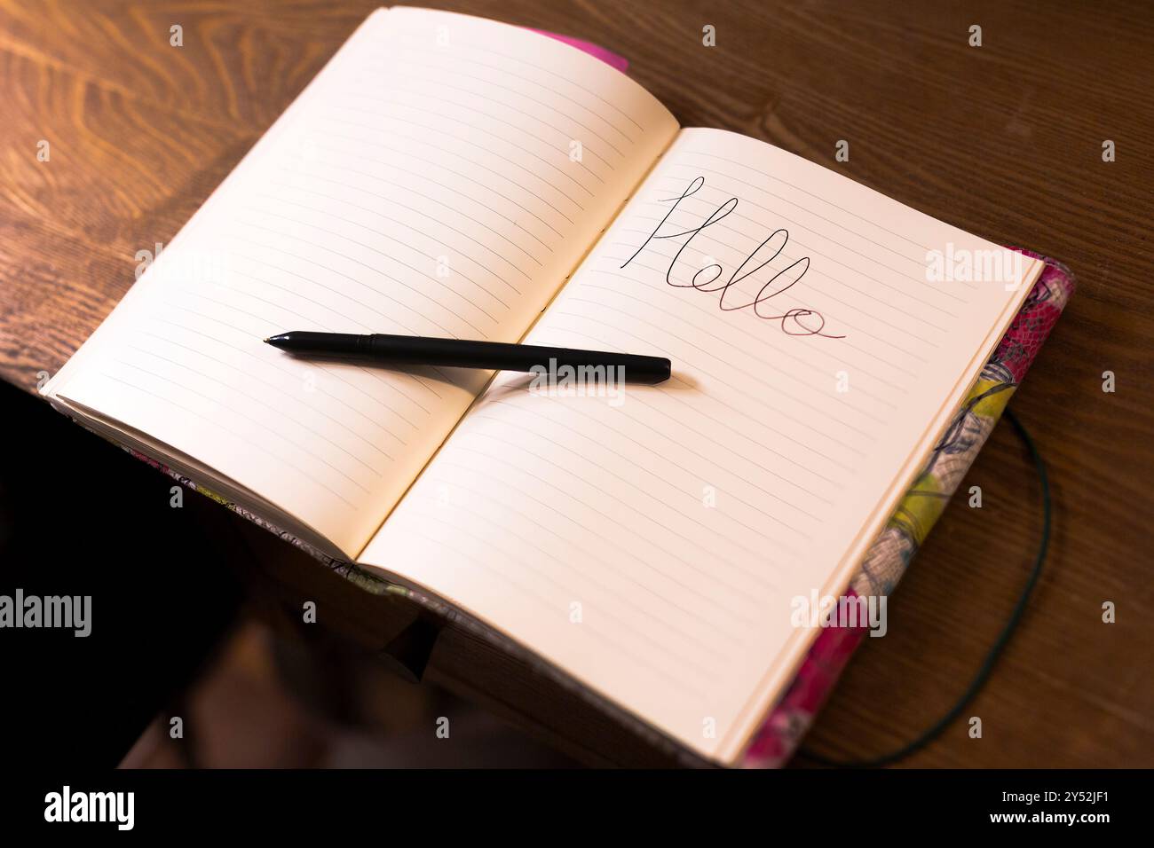 Un quaderno vuoto aperto su un tavolo di legno con una penna appoggiata accanto Foto Stock