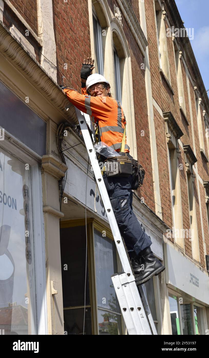 Tecnico telefonico su una scala che installa un nuovo ondulazione del cavo in fibra ottica Foto Stock
