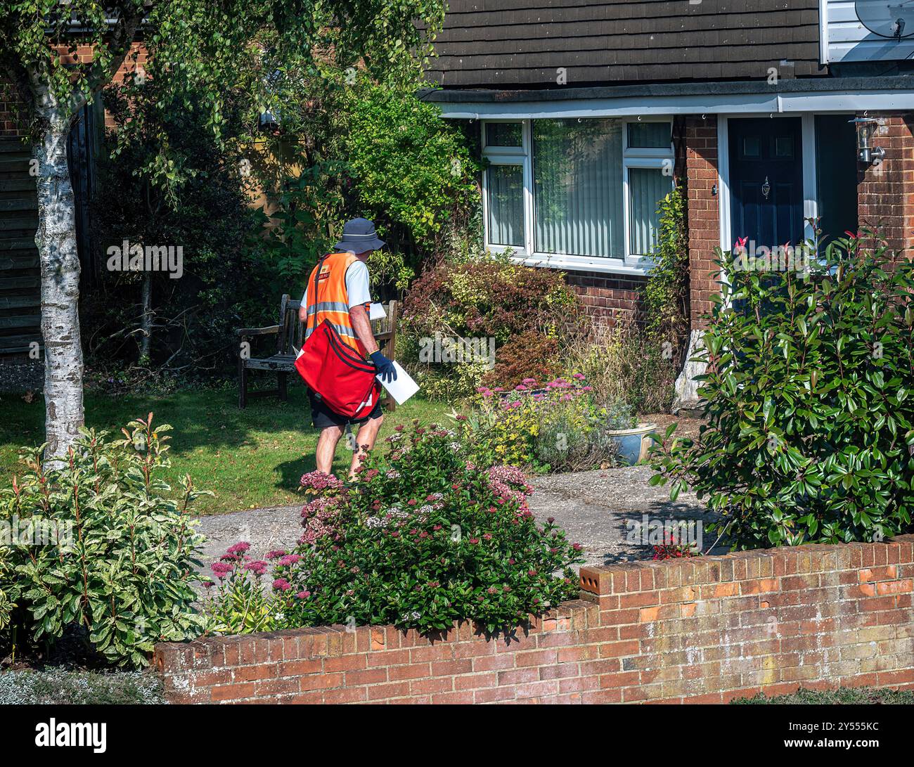 Postino in uniforme rossa brillante che consegna lettere a case in Inghilterra Foto Stock