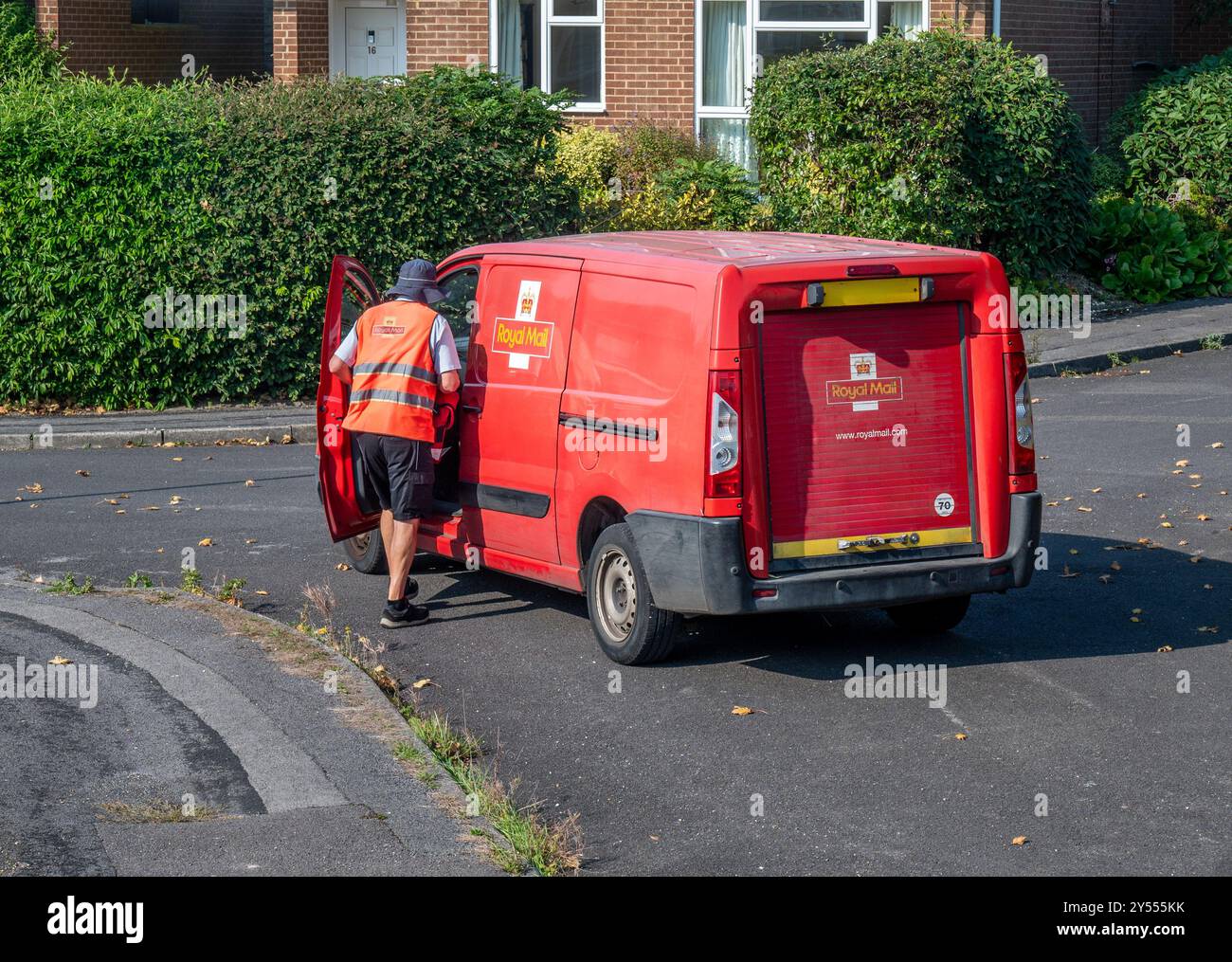 Postino in uniforme brillante salendo su un furgone postale dopo aver consegnato lettere a case nell'Hampshire, in Inghilterra Foto Stock