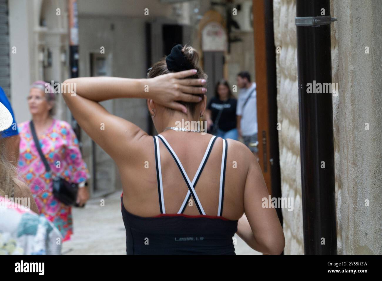 giovane donna attraente che cammina per le stradine del centro storico di bari vecchi su un top caldo e umido con cinturini a mano sui capelli che sembrano caldi e sudati Foto Stock