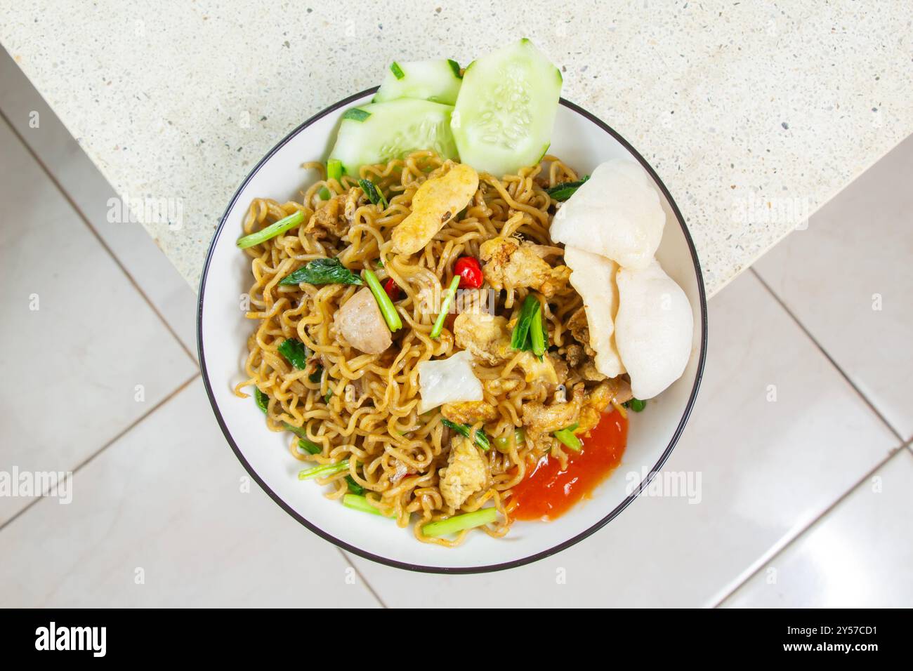 vista dall'alto degli spaghetti fritti ricoperti di pollo grattugiato, polpette, uova fritte su un piatto all'angolo di un tavolo di marmo Foto Stock