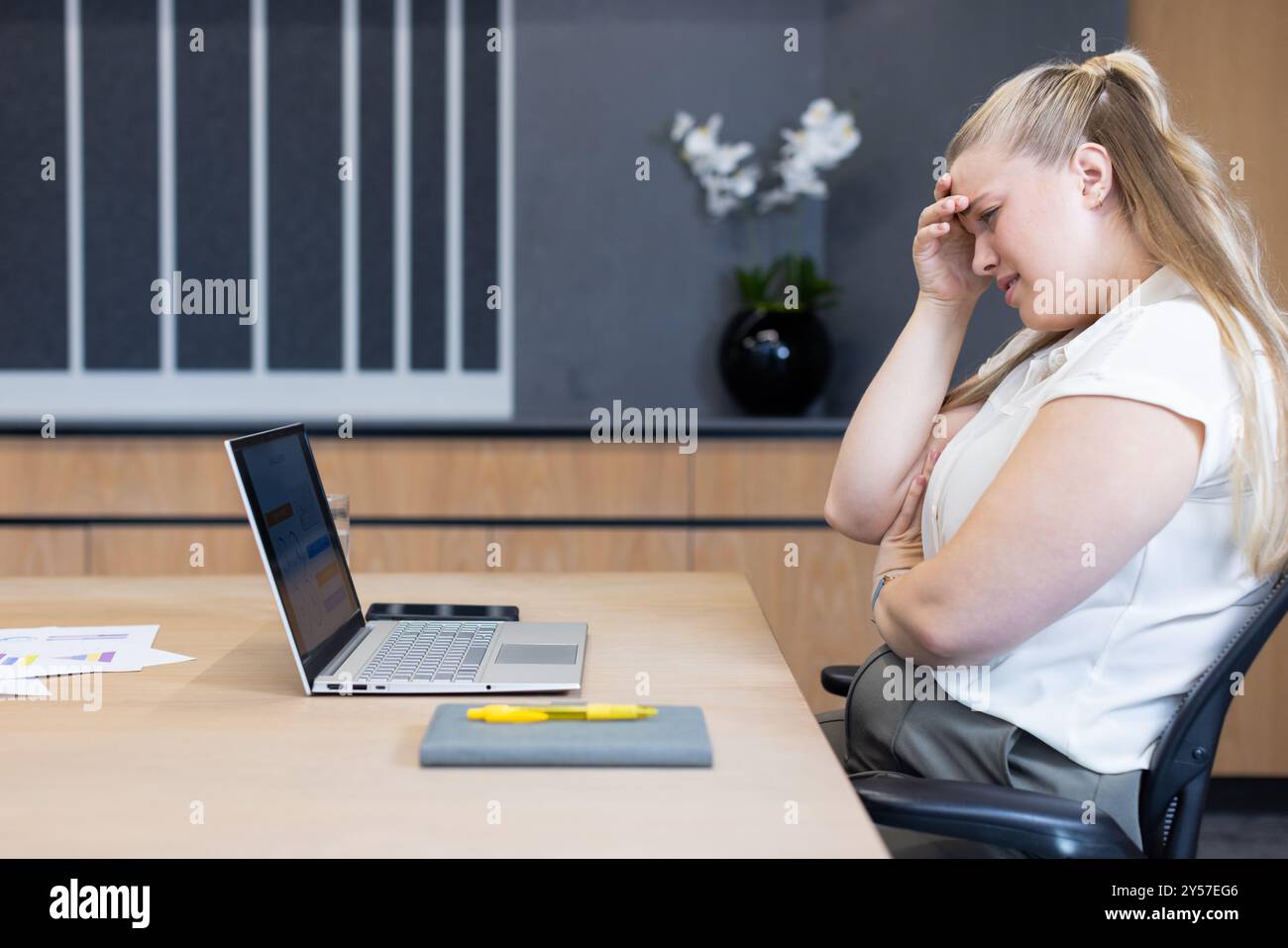 Donna d'affari stressata seduta alla scrivania con laptop e documenti in ufficio Foto Stock