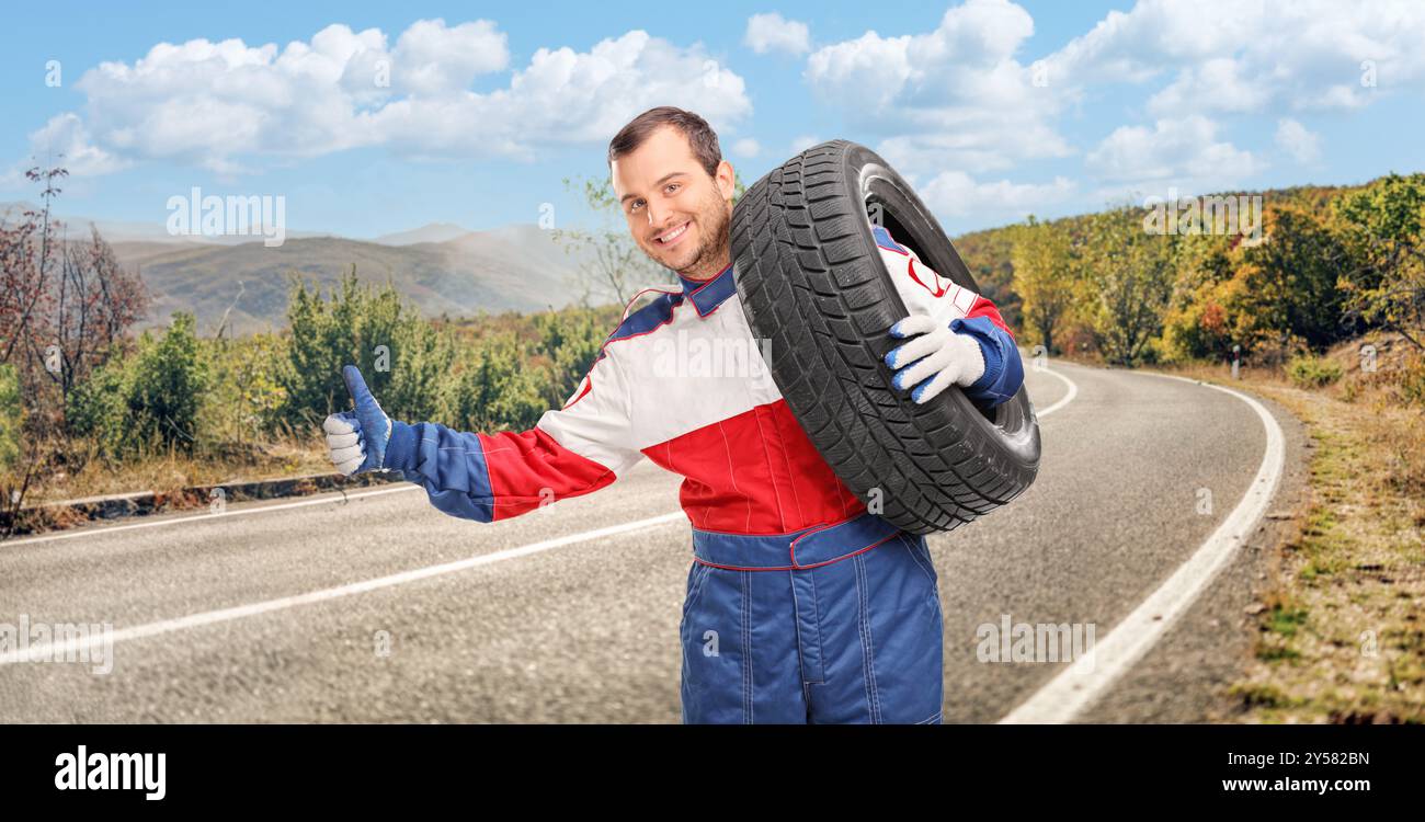 Pilota di auto che porta una gomma sulla spalla e autostop su una strada aperta Foto Stock