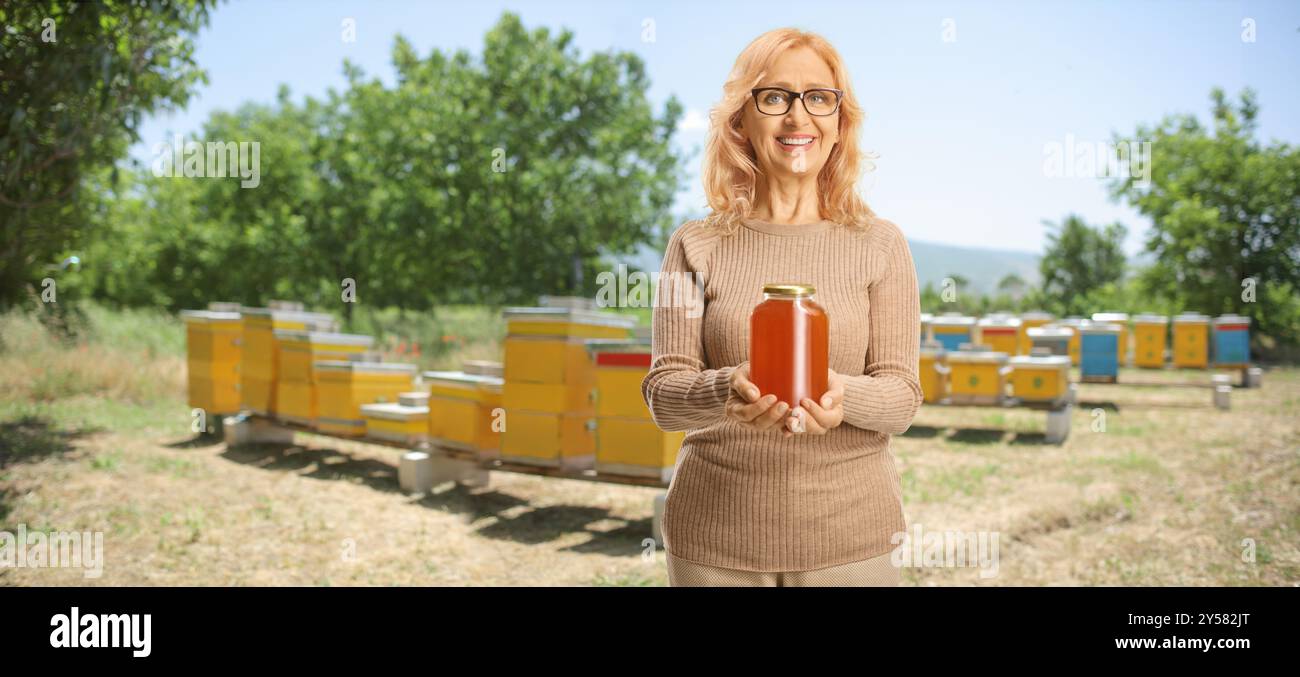 Donna di mezza età che tiene un vaso di miele in un allevamento di api Foto Stock