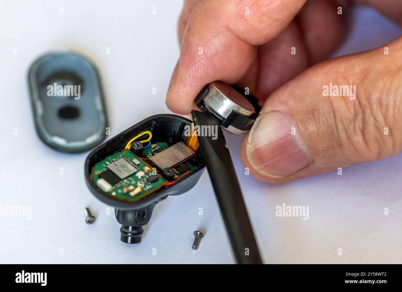Primo piano di un tecnico che utilizza uno strumento di plastica per sostituire la batteria di una cuffia wireless. Foto Stock