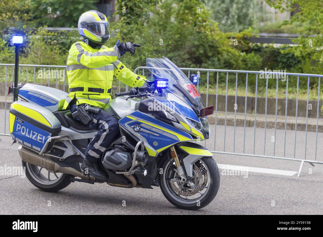 Un poliziotto in un gilet ad alta visibilità guida una moto della polizia con luci blu e mostra la strada su una strada a cordoncino, Stoccarda, Baden-Wuertt Foto Stock