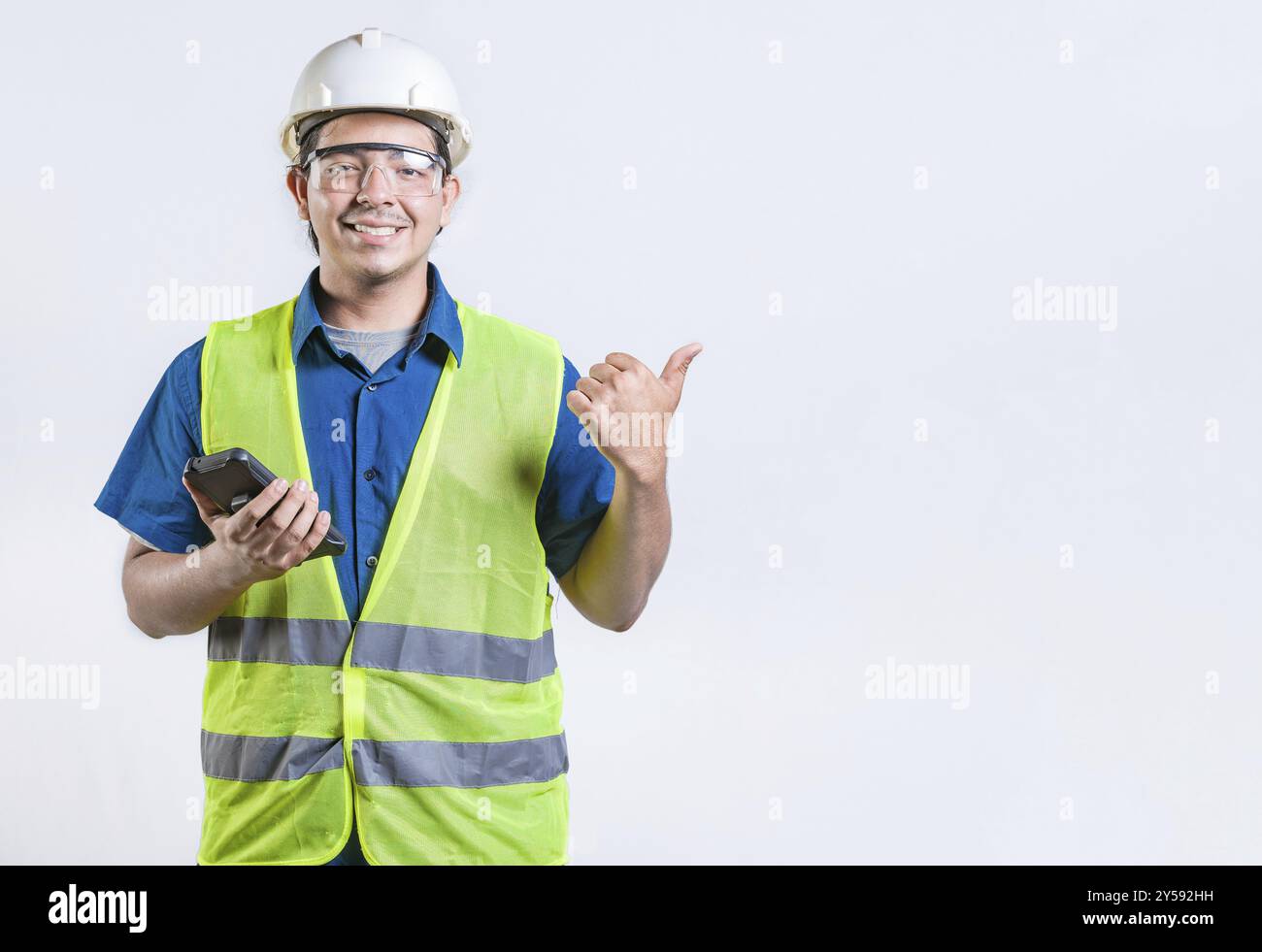 Giovane architetto con telefono che punta allo spazio vuoto isolato. Ingegnere sorridente che tiene il telefono e indica il lato isolato Foto Stock