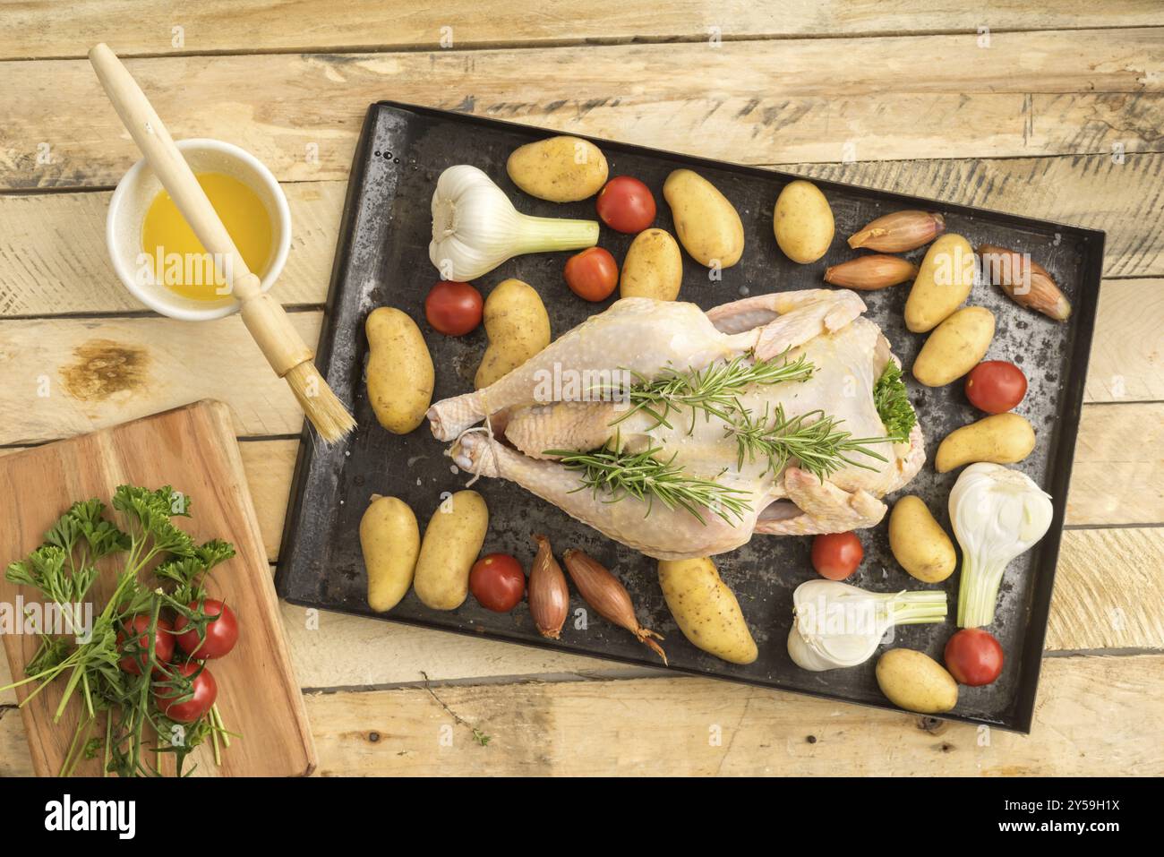 Pollo arrosto preparato per arrostire con aglio giovane, scalogni, prezzemolo, pomodori ciliegini, patate e olio d'oliva su un vassoio da forno Foto Stock