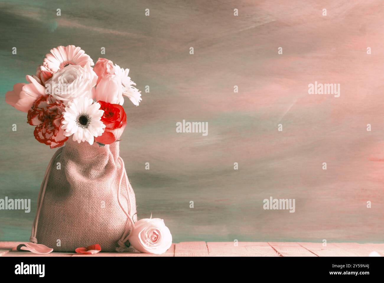 Bouquet di rose, tulipani e gerbera, avvolto in un sacco di iuta, su un tavolo di legno, con una rosa e petali vicino, in un'annata tonalità di tè e arancio Foto Stock