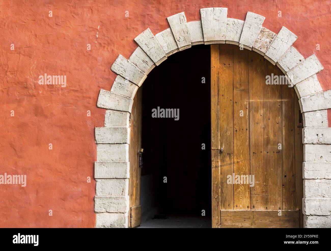 Antico ingresso ad arco con doppie porte in legno, lato sinistro aperto e l'arancione-rosa parete Foto Stock