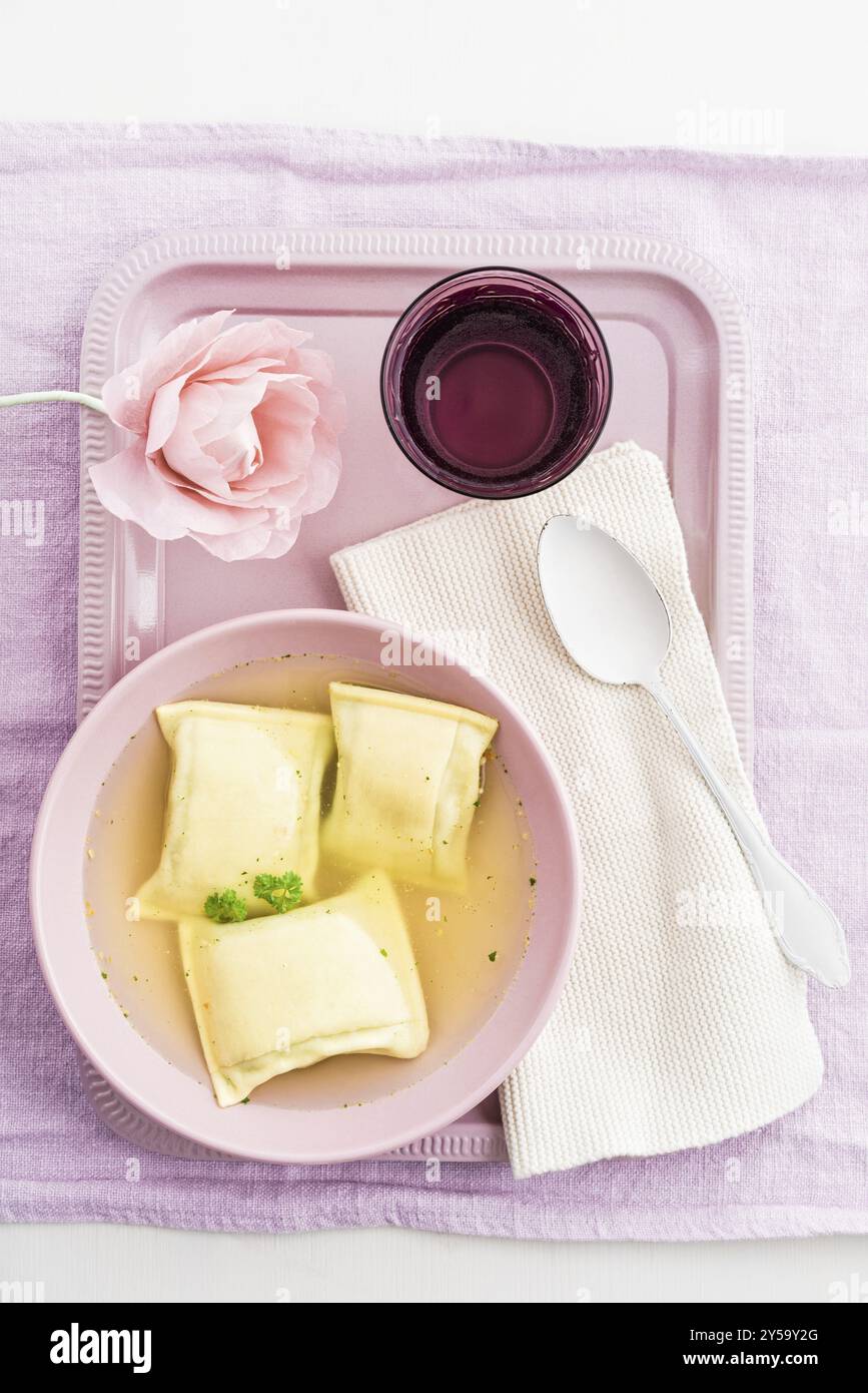 Maultaschen riempito quadratini di pasta in brodo con acqua e una carta crespa fiore su un vassoio Foto Stock