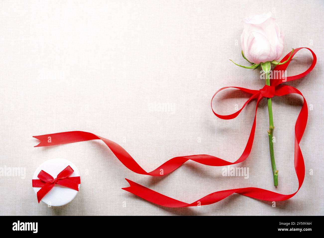 Biglietto d'auguri con una rosa legata con nastro rosso e fiocco e una confezione regalo bianca con fiocco, con spazio per un testo, su sfondo in tessuto vintage Foto Stock