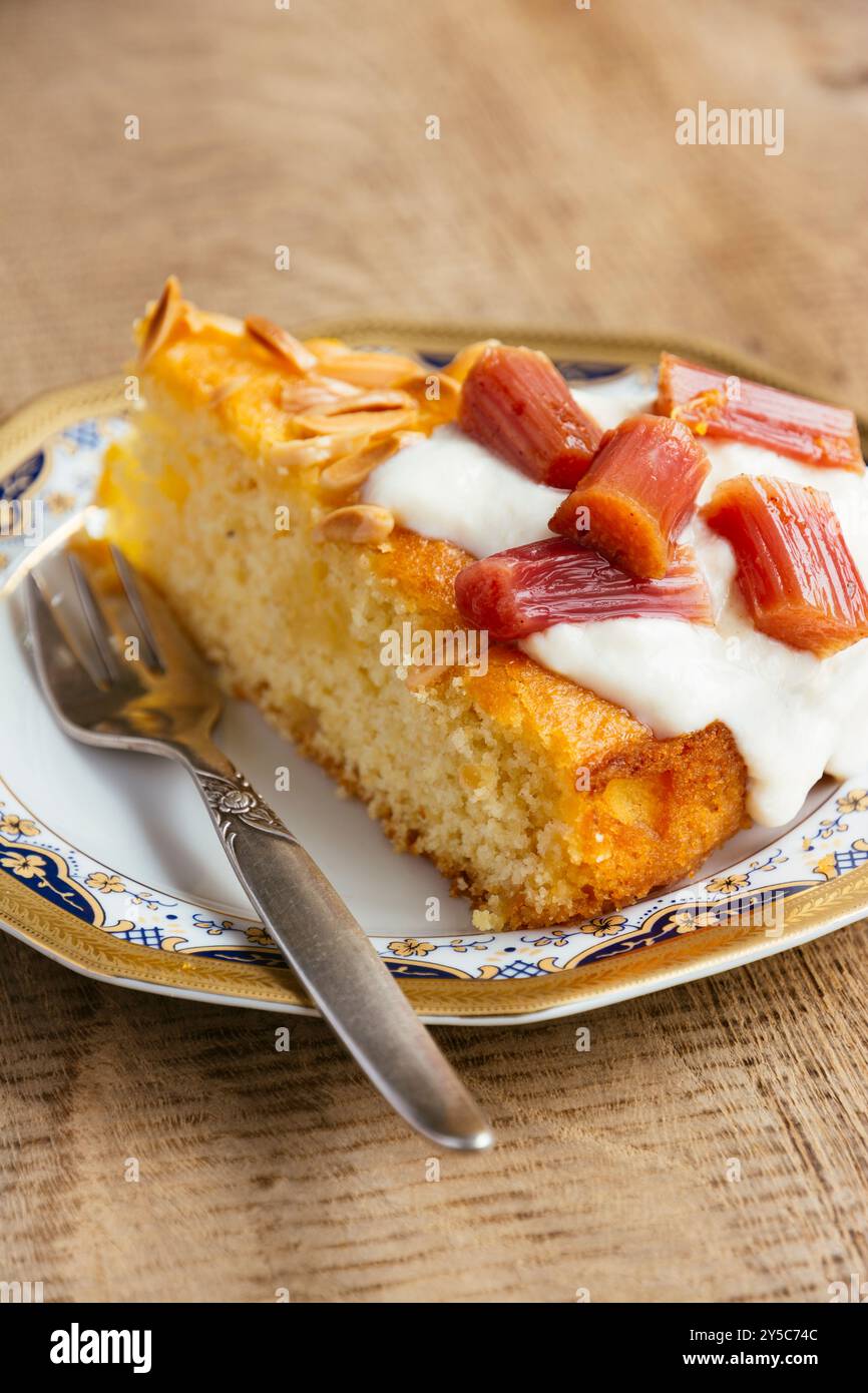 Torta di semola all'arancia e alle mandorle fatta in casa con rabarbaro al forno, servita con un cucchiaio di yogurt di soia e alcuni pezzi di rabarbaro. Foto Stock