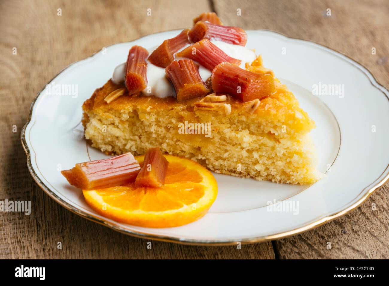 Torta di semola all'arancia e alle mandorle fatta in casa con rabarbaro al forno, servita con un cucchiaio di yogurt di soia e alcuni pezzi di rabarbaro. Foto Stock
