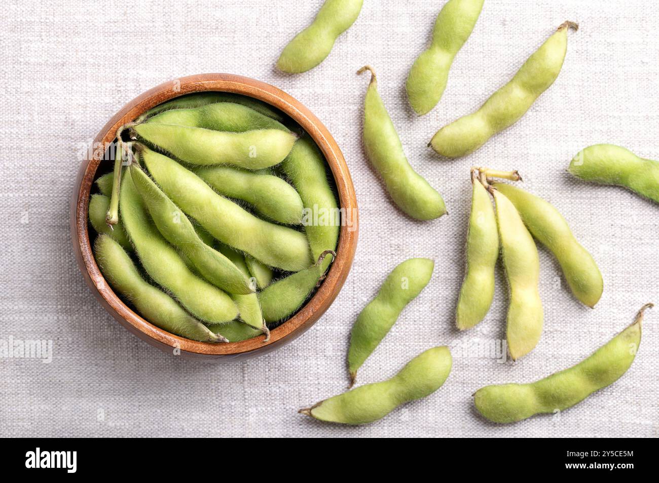 Edamame fresco, semi di soia verde nella cialda, in un recipiente di legno, su lino. Soia immatura cruda, glicina max, utilizzata bollita o al vapore e salata. Foto Stock