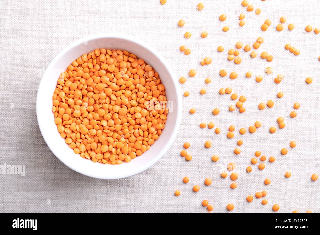 Lenticchie rosse in una ciotola bianca su lino. Varietà di lenticchie con buccia rimossa per un tempo di cottura più breve ed evitare di ammollo. Frutta secca di Lens culinaris Foto Stock