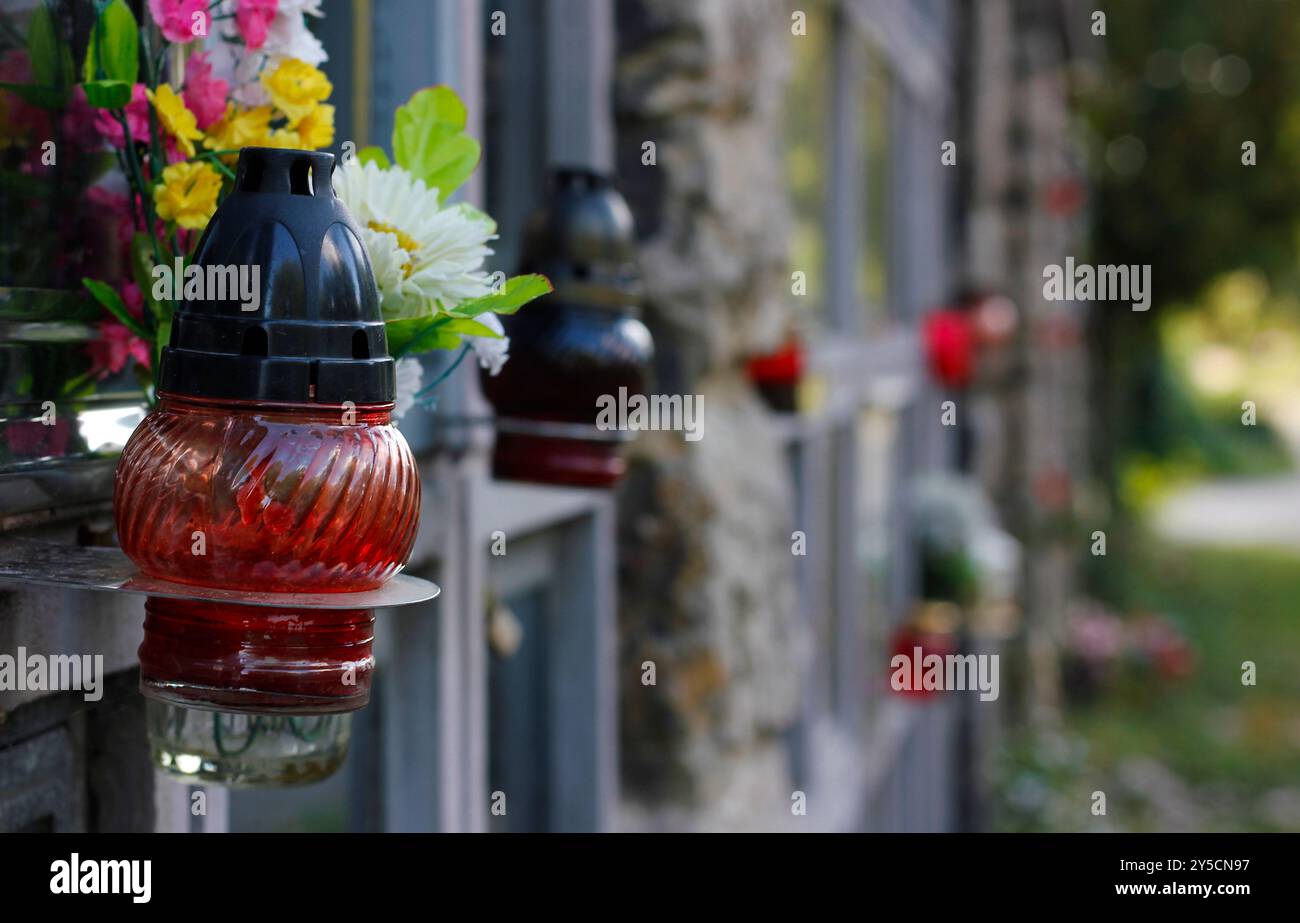 Primo piano di una candela e decorazione di fiori artificiali su una tomba nella parete del columbarium. Simbolo del ricordo dei nostri parenti deceduti. Festa di tutte le anime Foto Stock