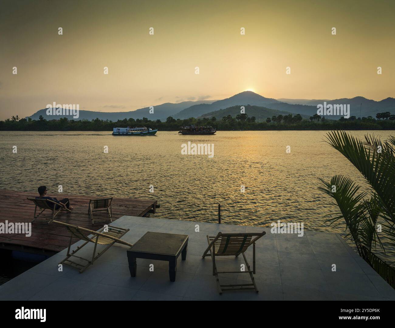 Vista del tramonto sul fiume a kampot cambogia asia con rilassanti sedie a sdraio e traghetti Foto Stock