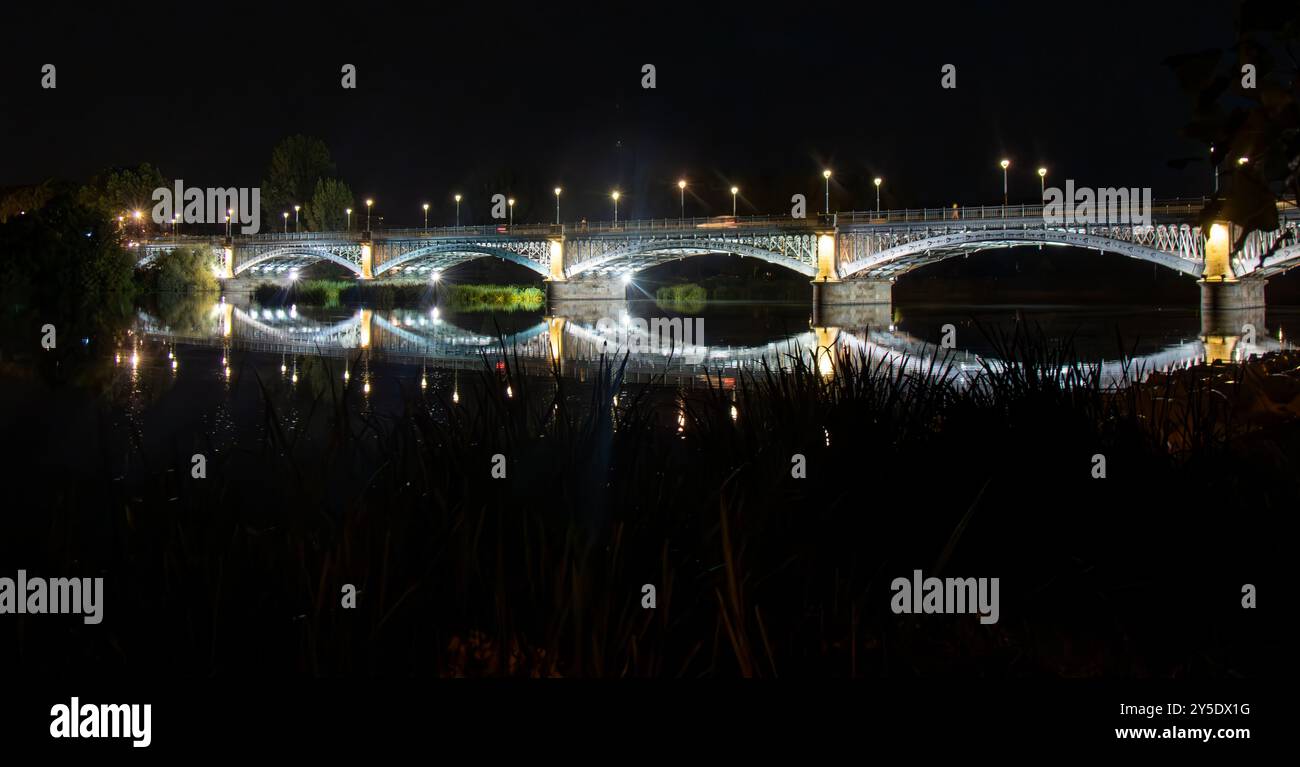 Fotografía nocturna del puente Enrique Estevan iluminado, reflejado en las Tranquilas aguas del Río Tormes. Salamanca, España Foto Stock