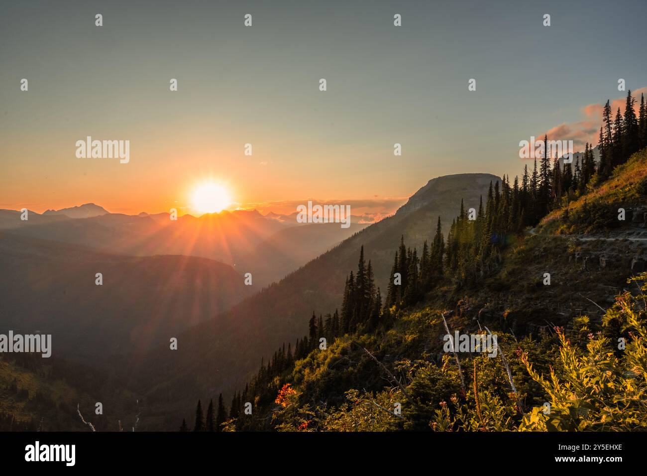 Il sole arancione si trova sotto il Continental divide in lontananza dall'Highline Trail nel Glacier National Park Foto Stock