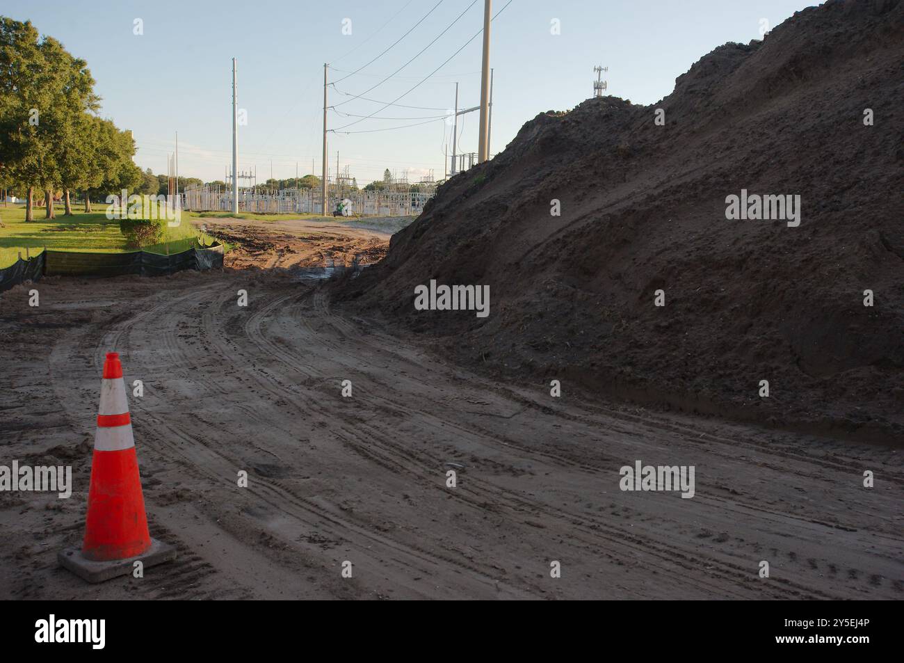 Ampia vista vicino a pali di terra linee principali piste di pneumatici vicino al tramonto grande sottostazione elettrica con linee ad alta potenza in Florida. Silt Fencing, erba verde, Foto Stock