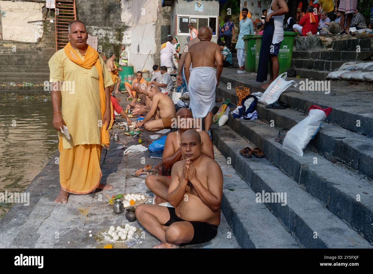 Un sacerdote indù (l) che conduce riti per i parenti defunti di uomini indù, questi ultimi con teste rituali rasate; a Banganga Tank, Mumbai, Ind Foto Stock