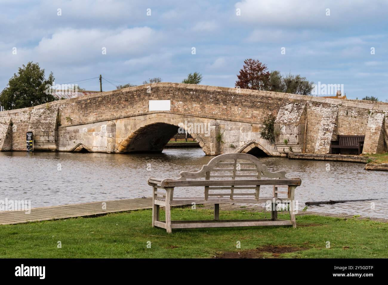 Panchina vuota da un ponte vecchio e basso sul fiume Thurne nel Norfolk Broads National Park. Potter Heigham, Norfolk, East Anglia, Inghilterra, Regno Unito, Regno Unito Foto Stock